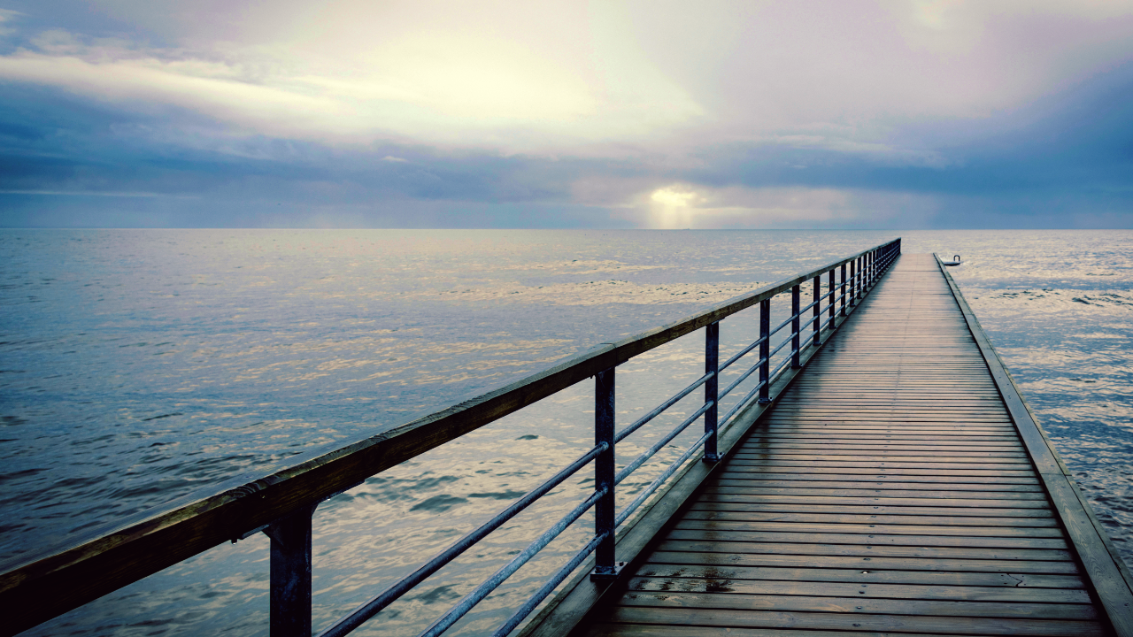Image of a pier with sea and clouds in the horizon.