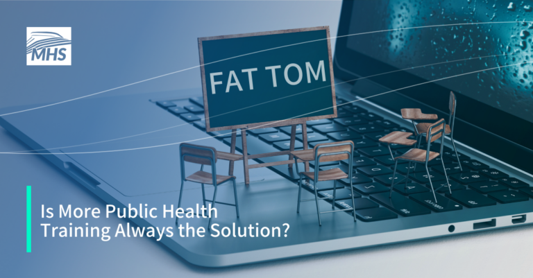 An image featuring a small chalkboard with the anagram FAT TOM written on it, surrounded by miniature desks and chairs placed on a laptop keyboard symbolizing public health training, with the words, Is More Public Health Training Always the Solution?