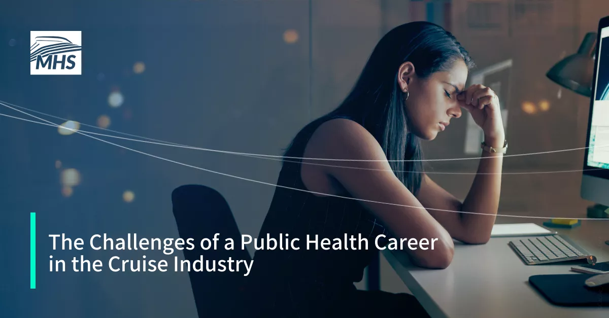 An image of a young businesswoman looking stressed while using a computer at night in a modern office with the words, The Challenges of a Public Health Career in the Cruise Industry
